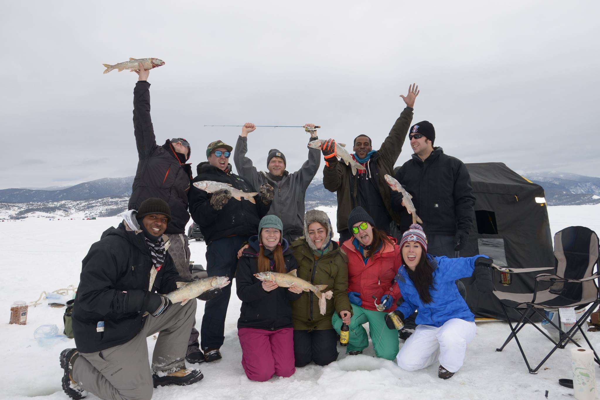 group of friends holding up the fish they caught while ice fishing on Colorado lake